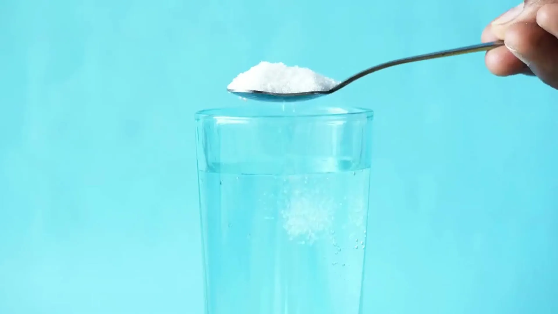 Una cuchara disuelve polvo blanco en un vaso de agua que se vuelve lechosa
